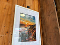 Framed poster of a scenic landscape with 'tregonhawke' text on a wooden wall.
